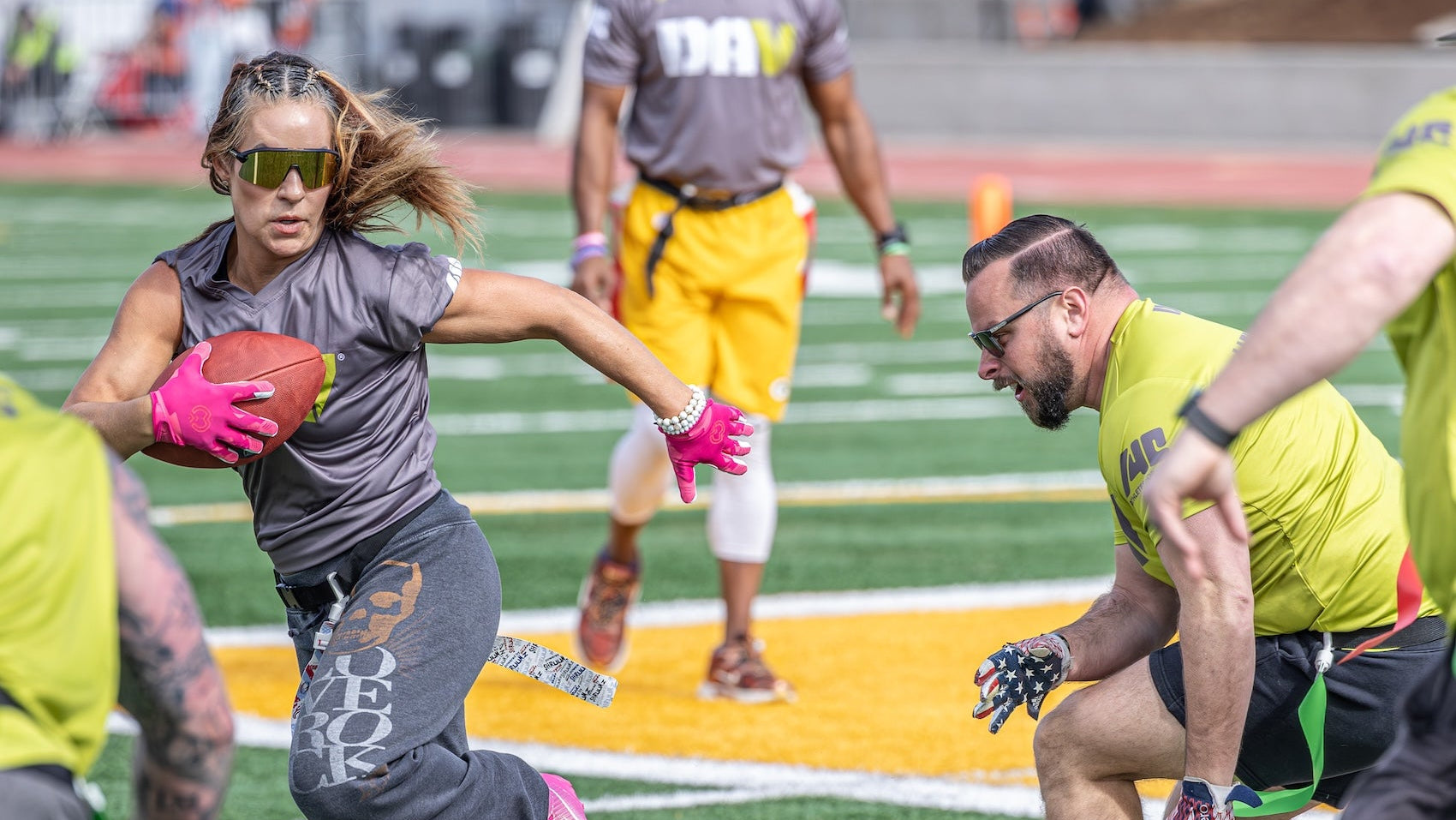 Woman in sports gear running with a football on a field, surrounded by other people.