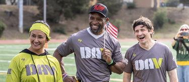 Three people standing together on a sports field, smiling and holding flags.