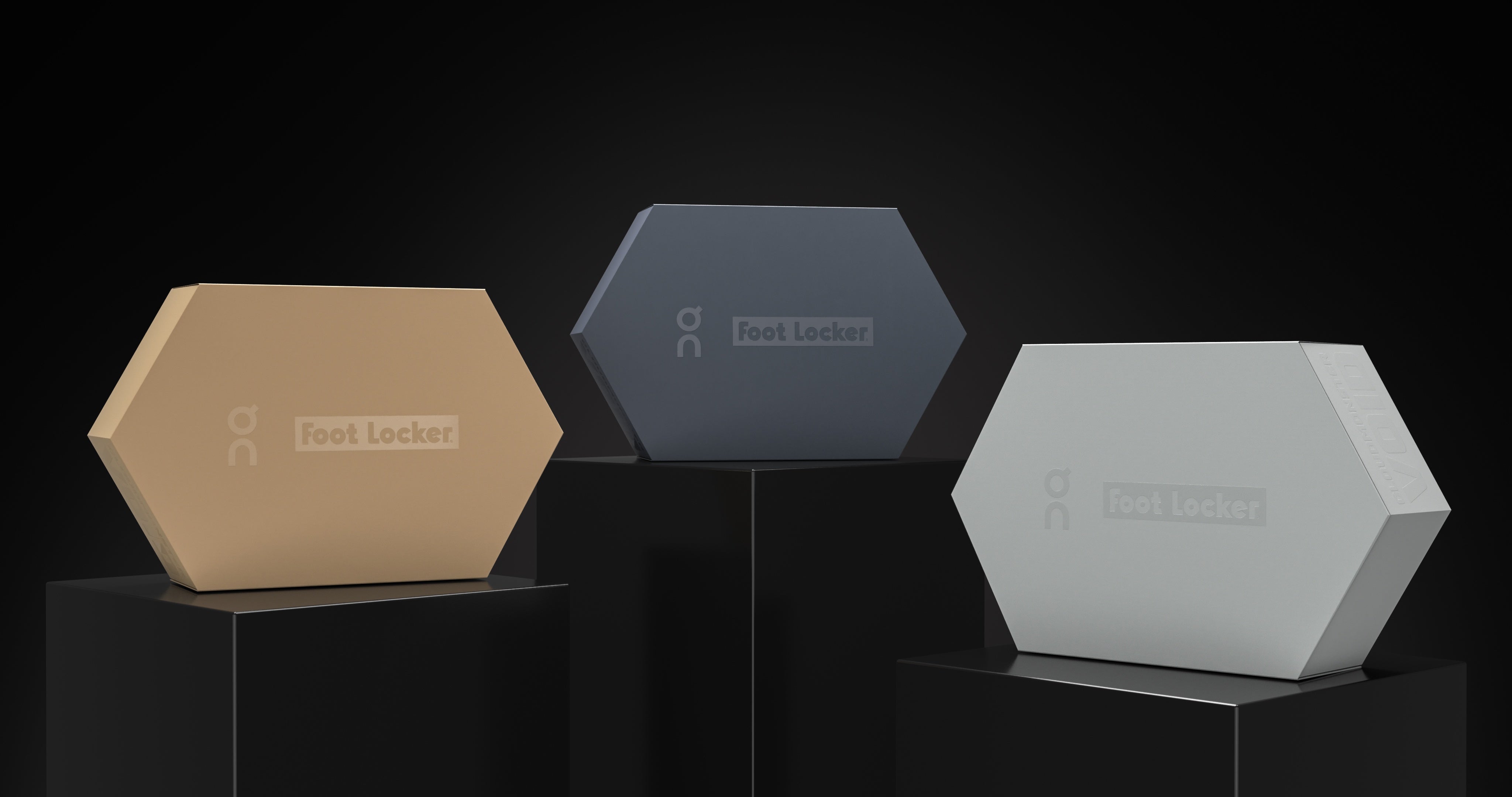 Three hexagonal Foot Locker boxes in tan, dark grey, and light grey on black pedestals.