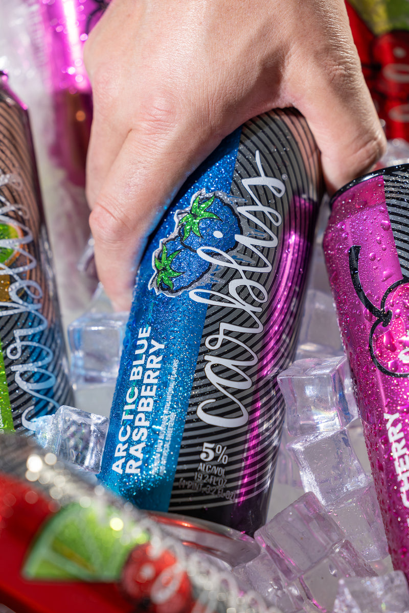 Hand holding a Carlsberg Arctic Blue Raspberry beer can with ice cubes and other cans in the background.