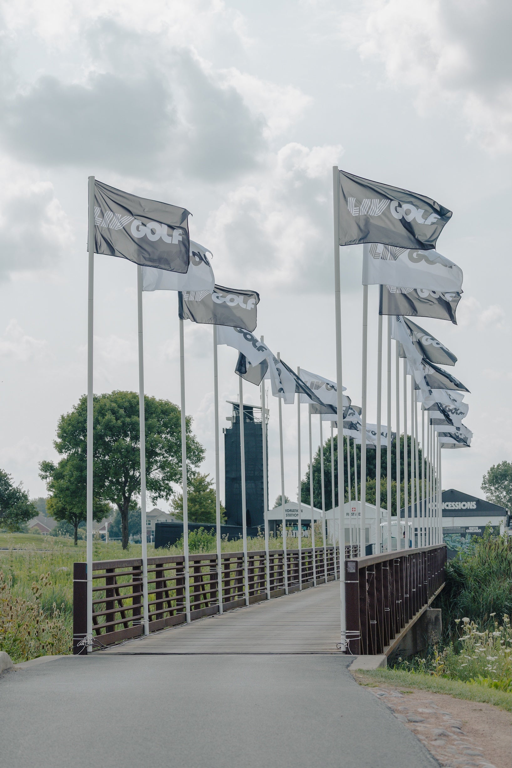 Bridge with mirrored surface reflecting multiple flags and buildings under a cloudy sky.