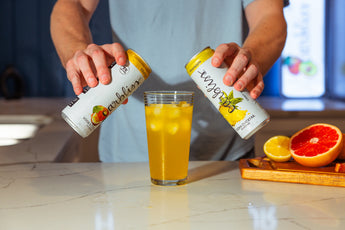 Man pours two sparkling vodka cocktails from cans into a glass with ice.