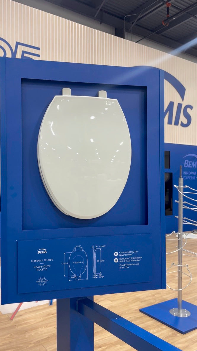 White toilet seat display in a blue frame with visible branding on a wall.