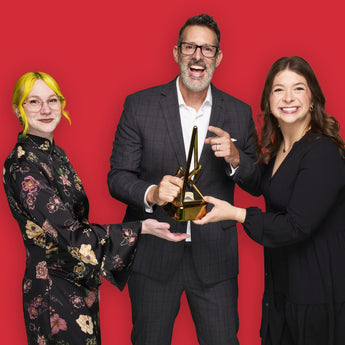 Justin Webb, Ashley Vogel, and Alyssa Gabrielse, posing with a Gold 2025 Anthem trophy against a red background 