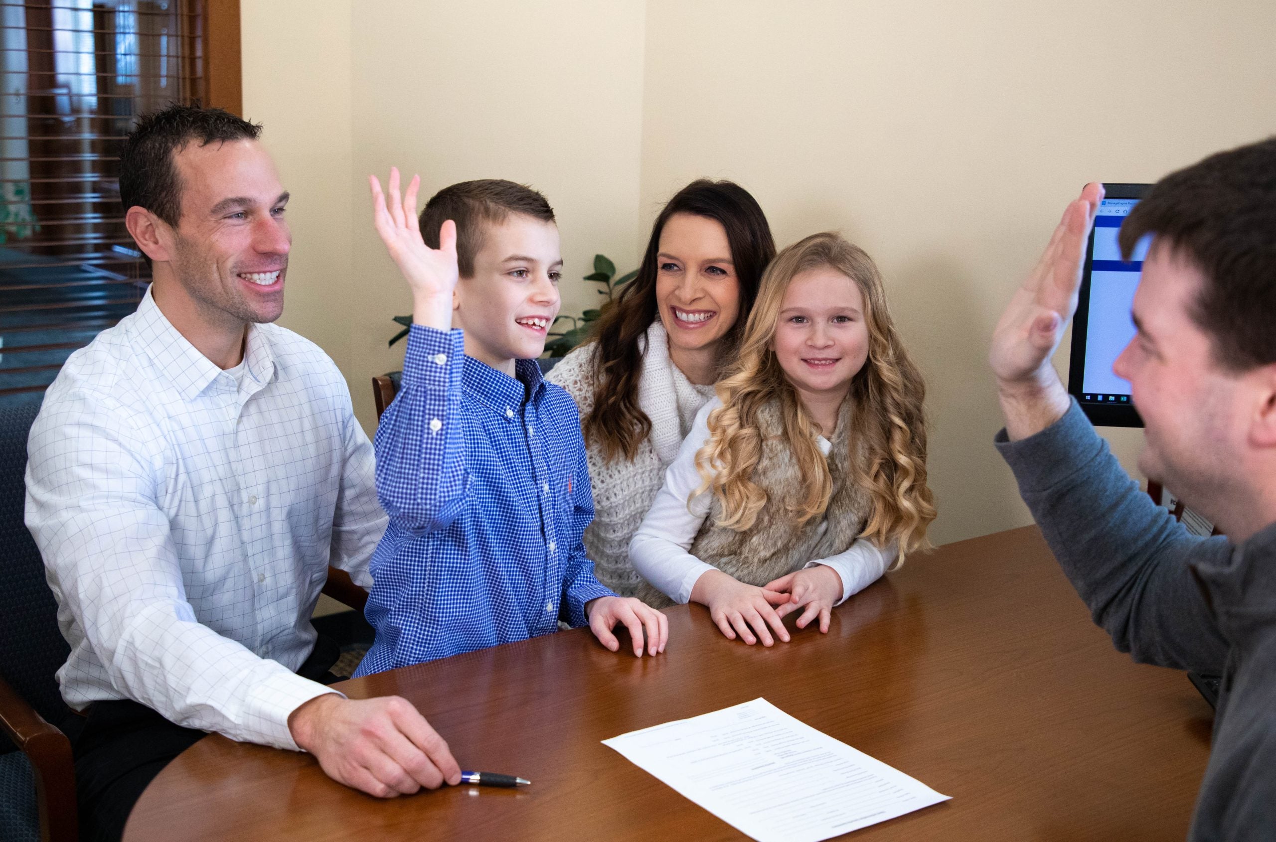 Family with two children high-fiving across a table with documents and a computer.