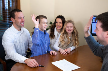 Family with two children high-fiving across a table with documents and a computer.