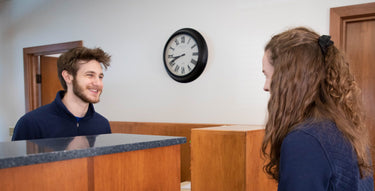 Man and woman talking at a reception desk with a clock on the wall.