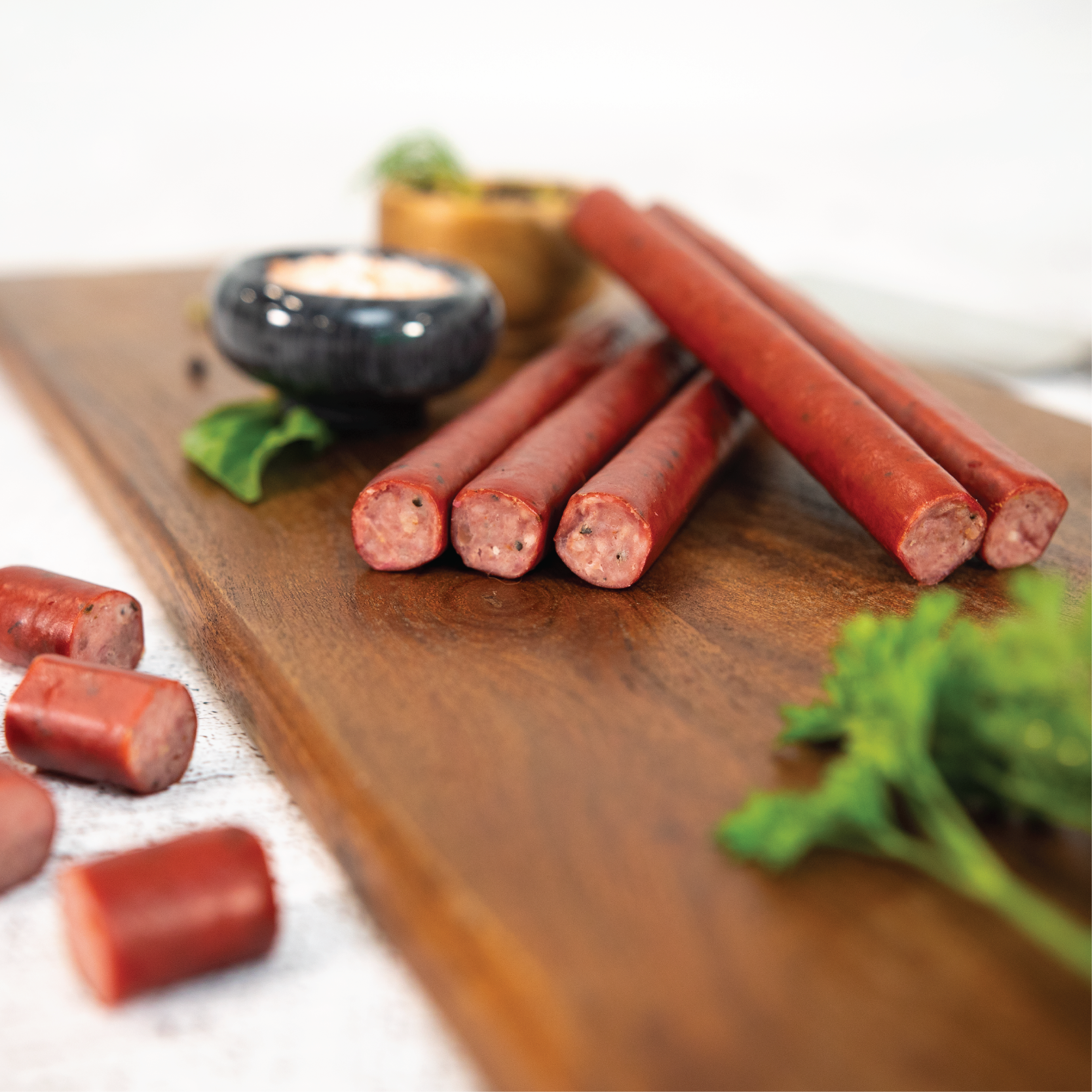 Hot dogs on a wooden cutting board with vegetables and a small bowl in the background.