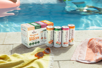 Carbliss Tropical Bliss vodka cocktail variety pack and cans on a poolside patio with towels and sunglasses.