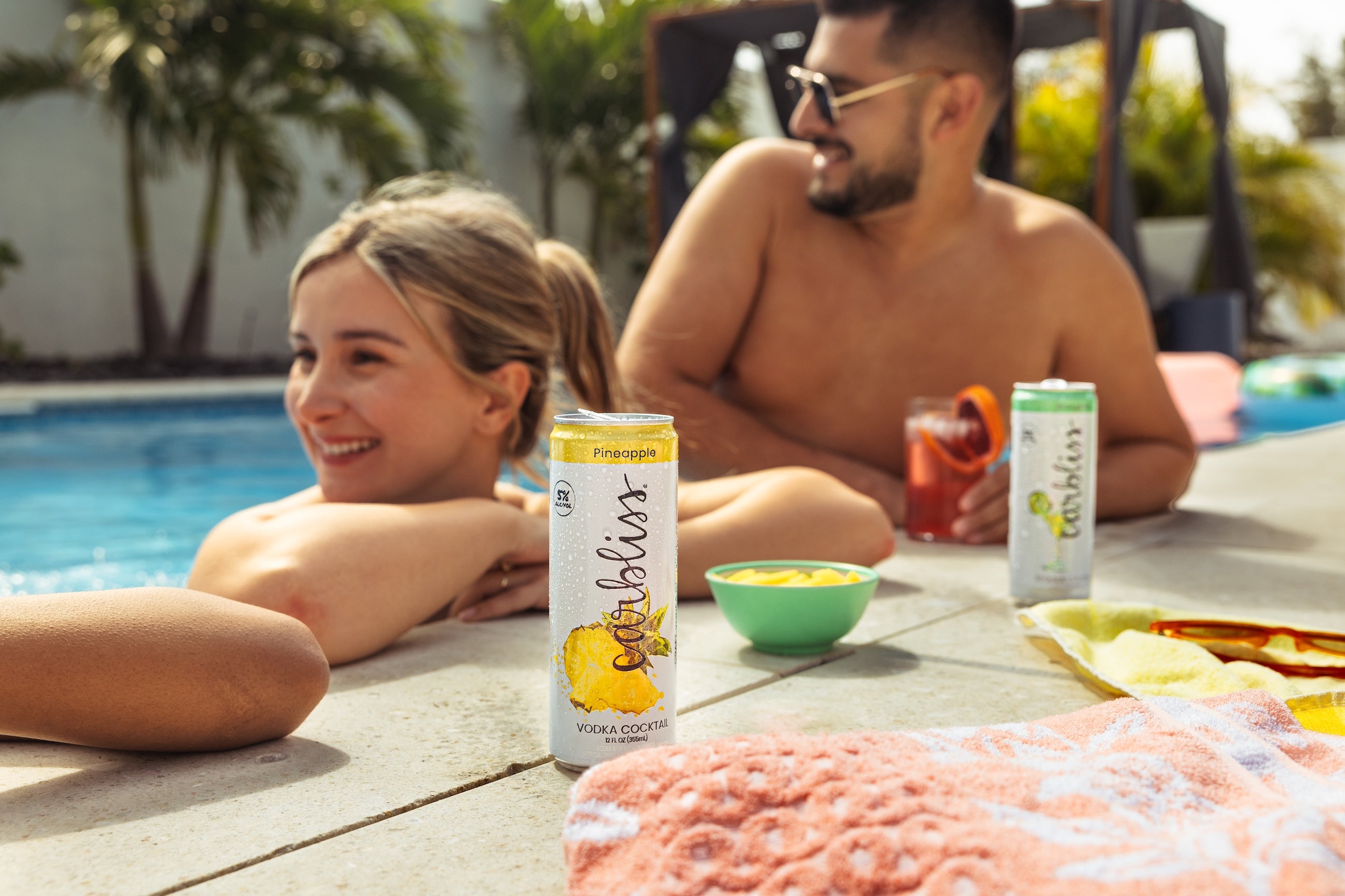 Couple relaxing by a pool with pineapple vodka cocktails and snacks.