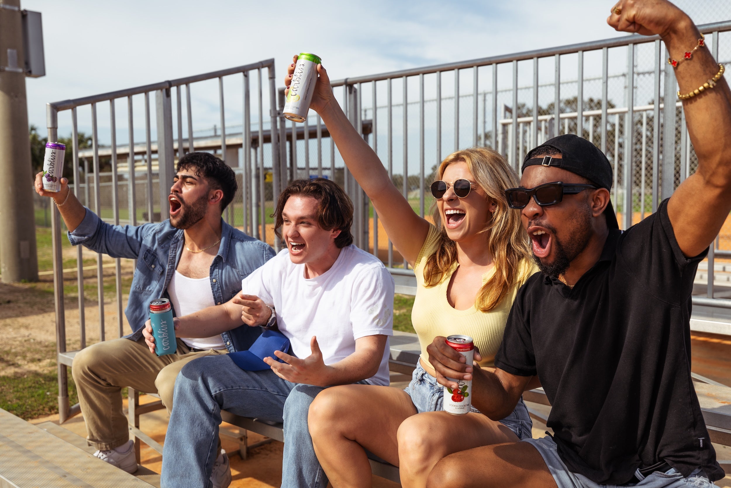 Friends cheer at a sporting event, holding cans of Carbliss vodka cocktails.