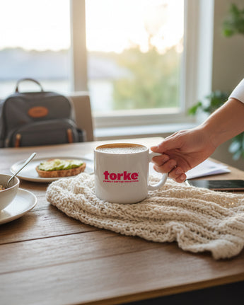Person holding a mug with 'torke' branding on a wooden table with a scenic view.