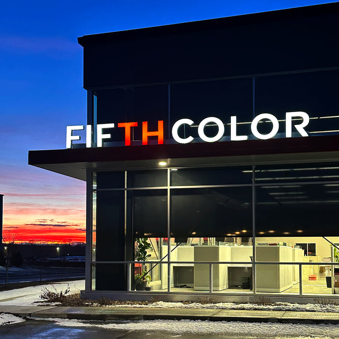 Glowing "FIFTHCOLOR" sign on modern building at dusk with vibrant sunset sky.