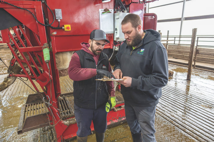 Farmers in a barn review notes next to a red dairy cow hoof trimming machine.