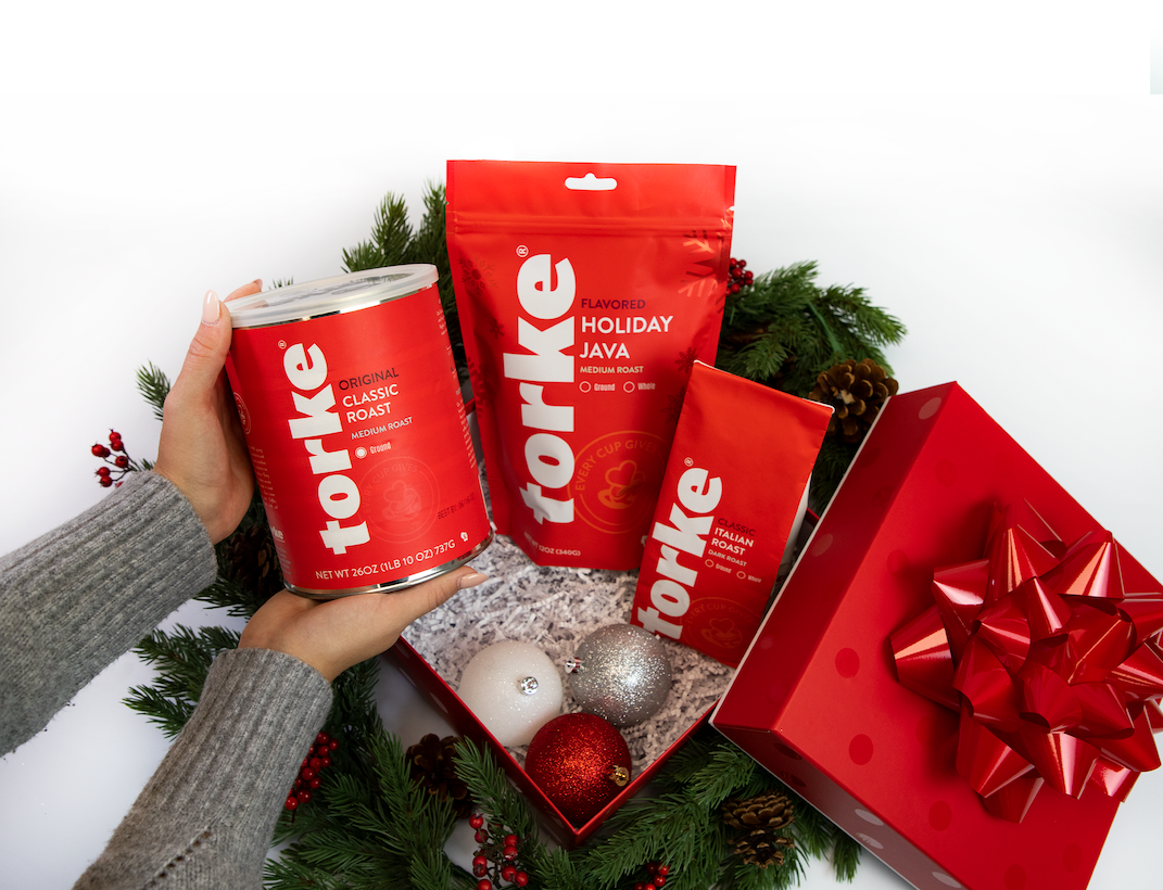 Person holding a can of Forke coffee next to holiday-themed coffee packages and a gift box with a bow.