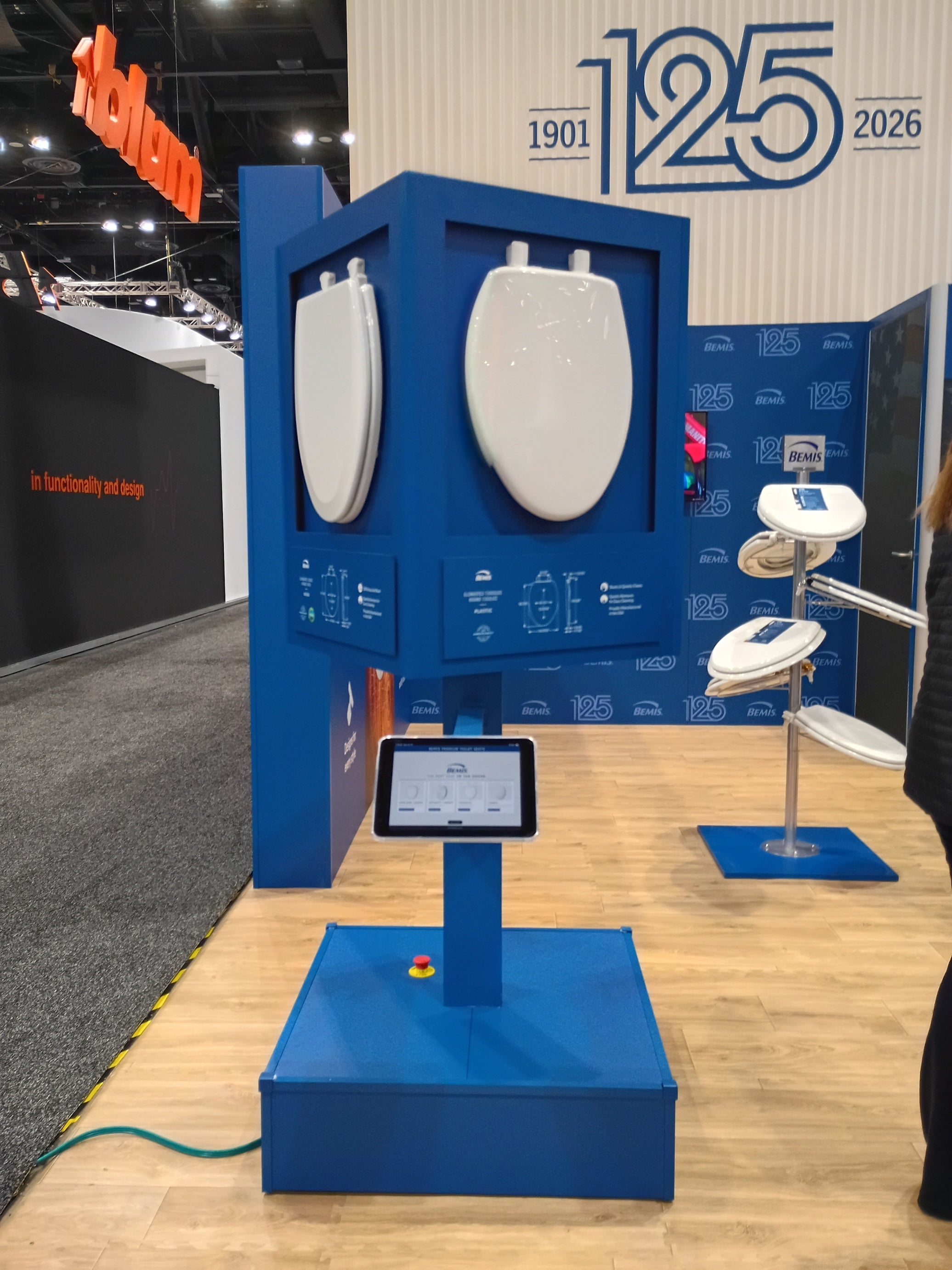 Display of toilet seats with a tablet on a blue stand at an exhibition.
