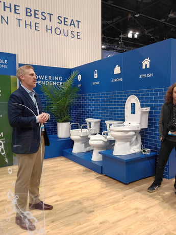 Two people standing in front of a display of toilets with promotional text on a blue wall.