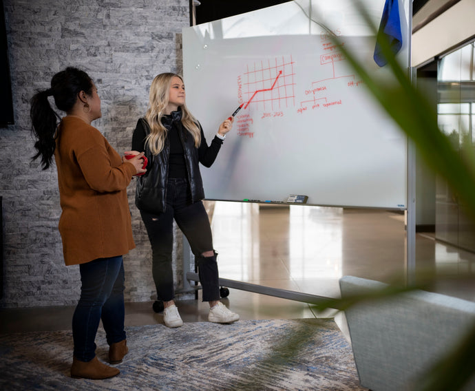 Two women discussing a graph on a whiteboard in an office setting.