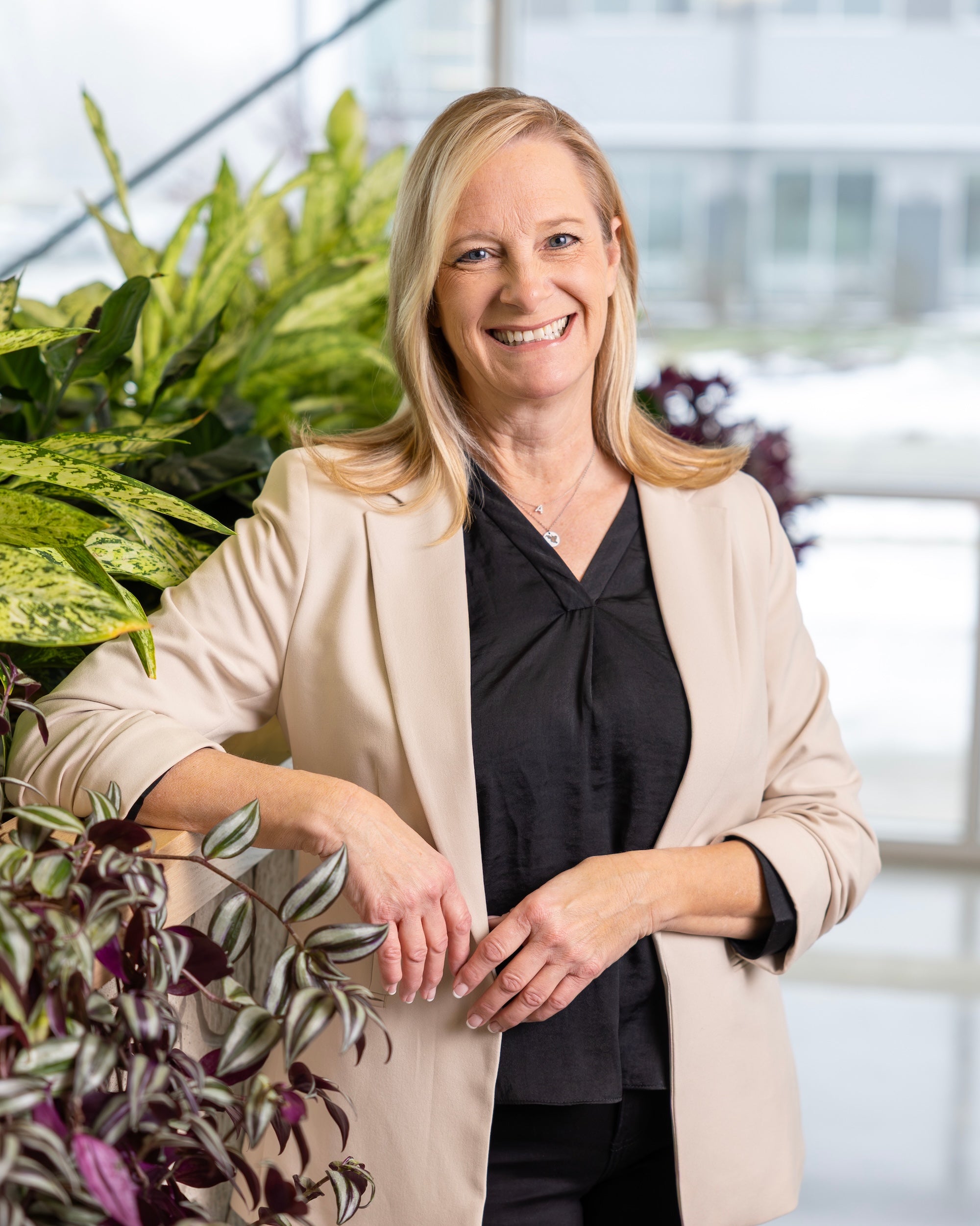 Woman in a beige blazer standing among plants indoors