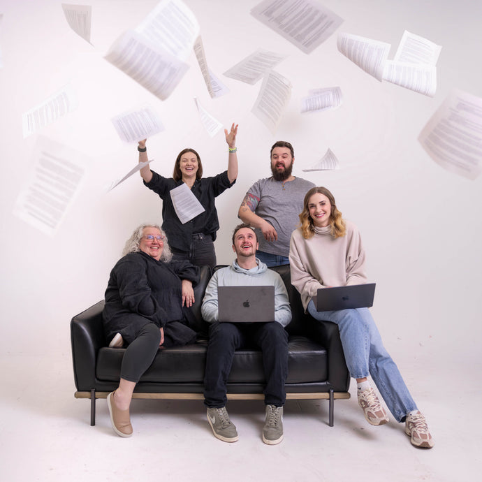 Five people sitting on a couch with laptops, surrounded by floating papers against a white background