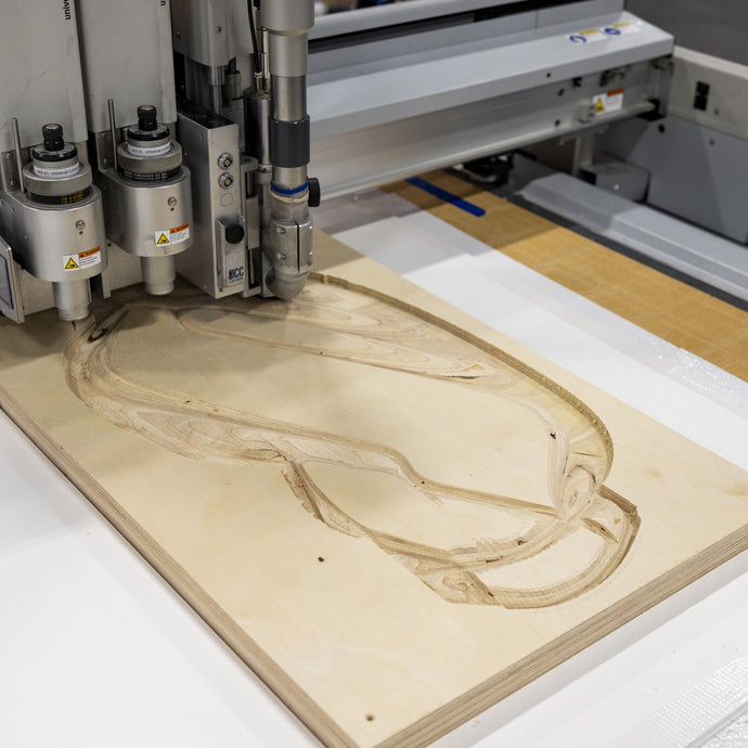 CNC router carves design into plywood sheet, close-up view.