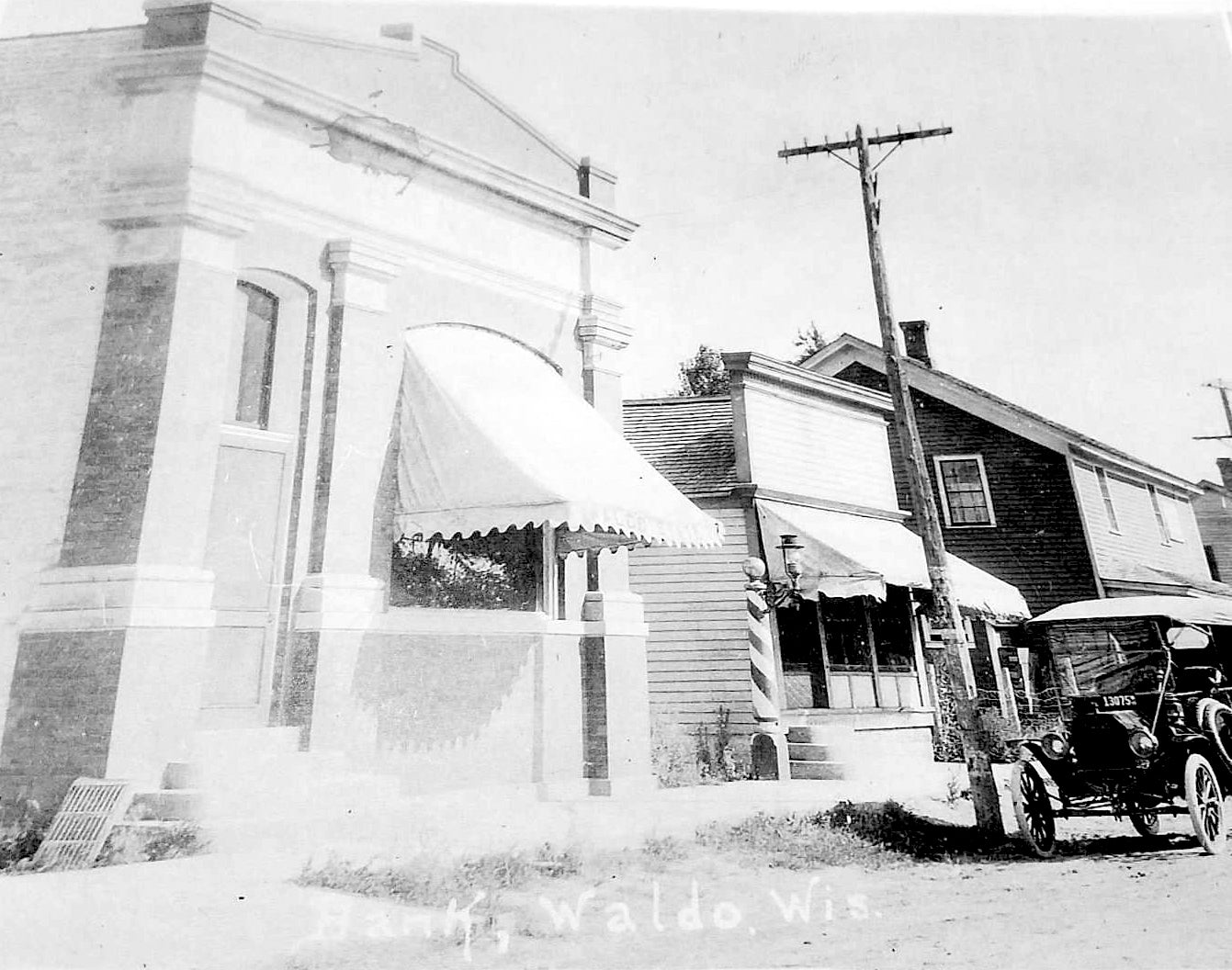 Vintage black and white photo of a street scene with a building, car, and telephone pole.