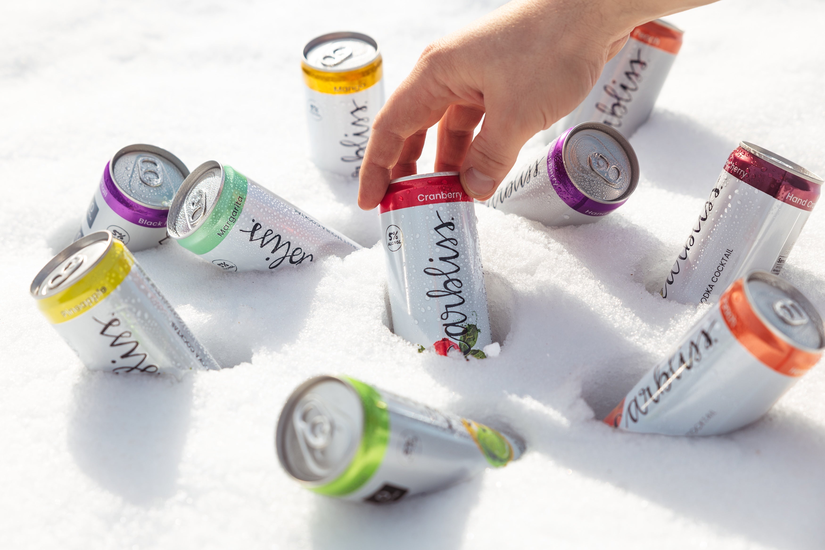 Cans of Carlsberg beer in various flavors on a snowy surface with a hand reaching for one can.