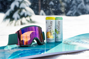 Snowboard with goggles and two cans of Criciublas on a snowy background