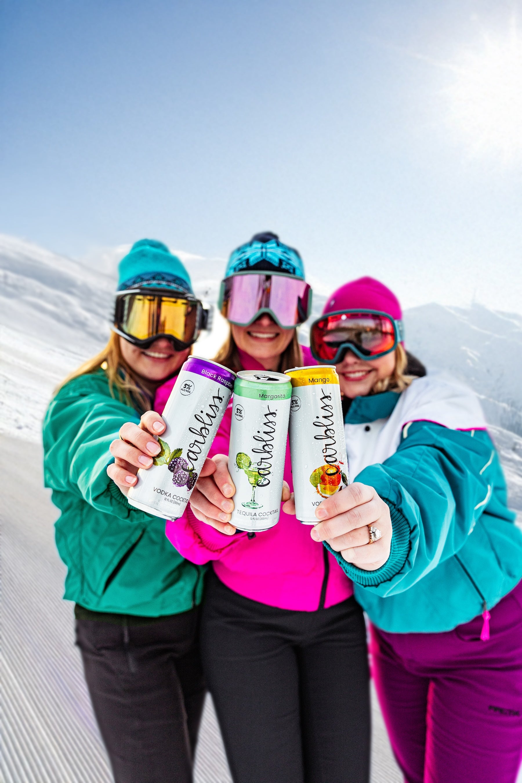 Three people in winter gear holding cans of a brand with a snowy mountain background