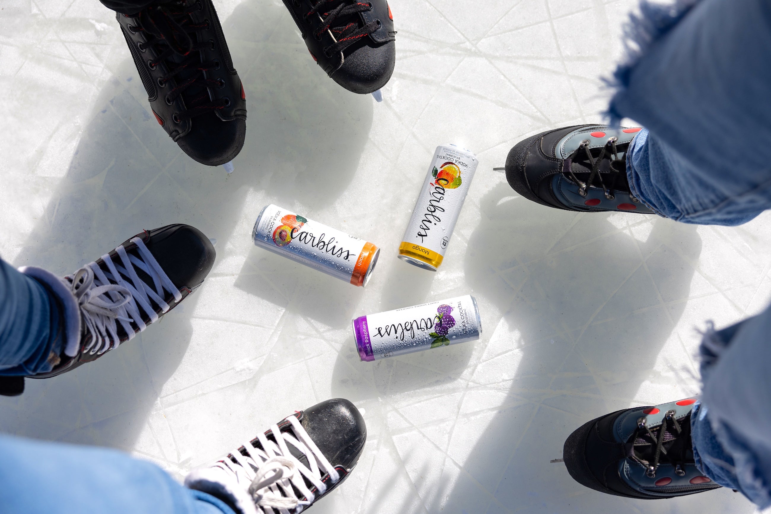 Four people's feet wearing shoes on a white surface with colorful energy drink cans.