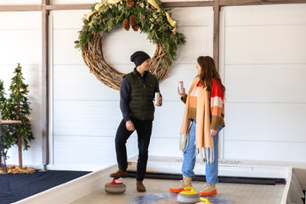 Two people on an indoor curling rink with a decorative wreath on the wall.