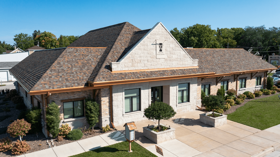 Two-story house with a gray roof and stone facade, surrounded by greenery.